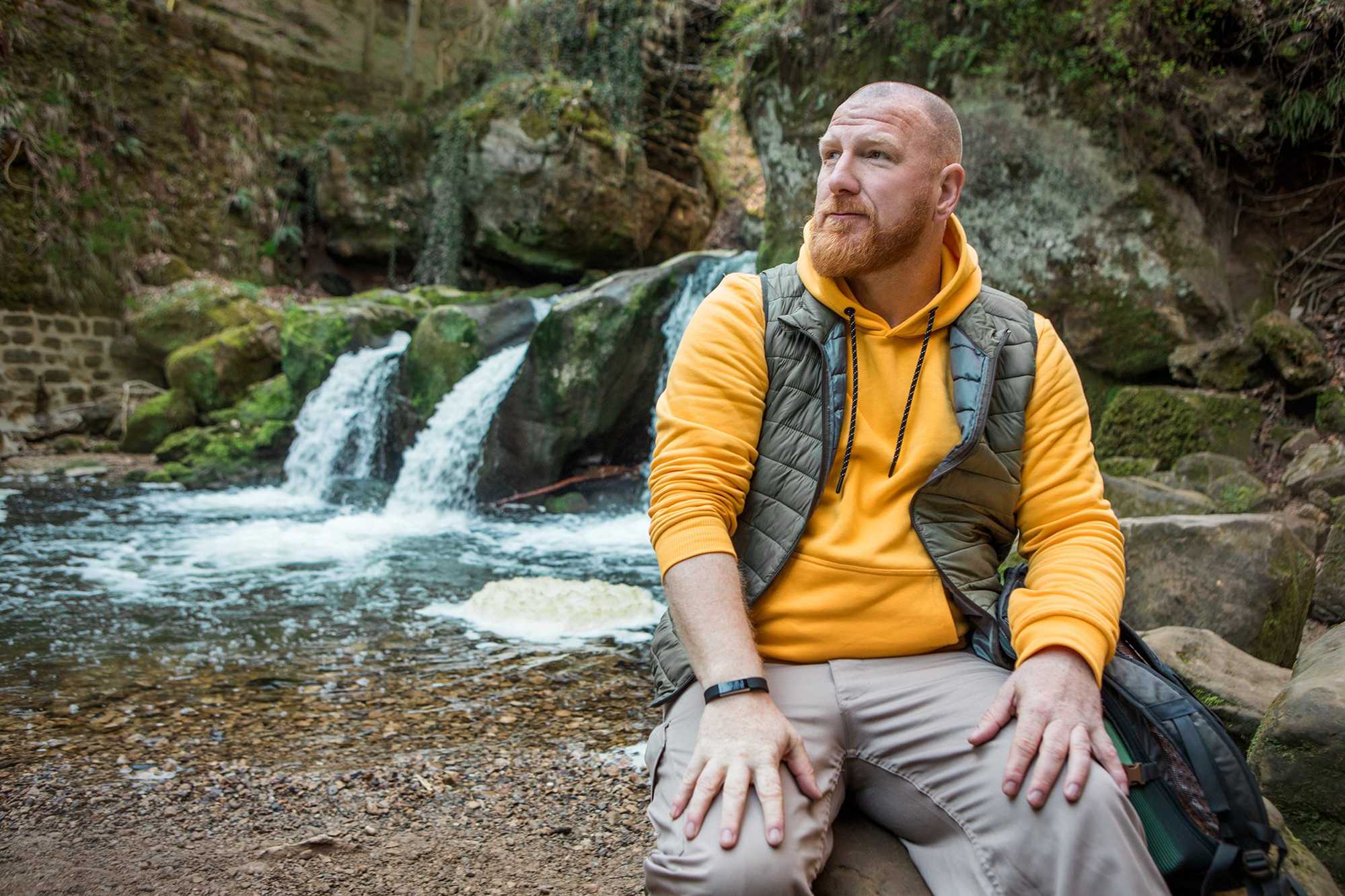 Man with beard sits on rock near waterfalls Man with beard sits on rock near waterfalls